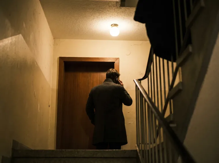 Ausgesperrte Person steht nachts im Treppenhaus vor der verschlossenen Wohnungstür und telefoniert mit dem Notdienst